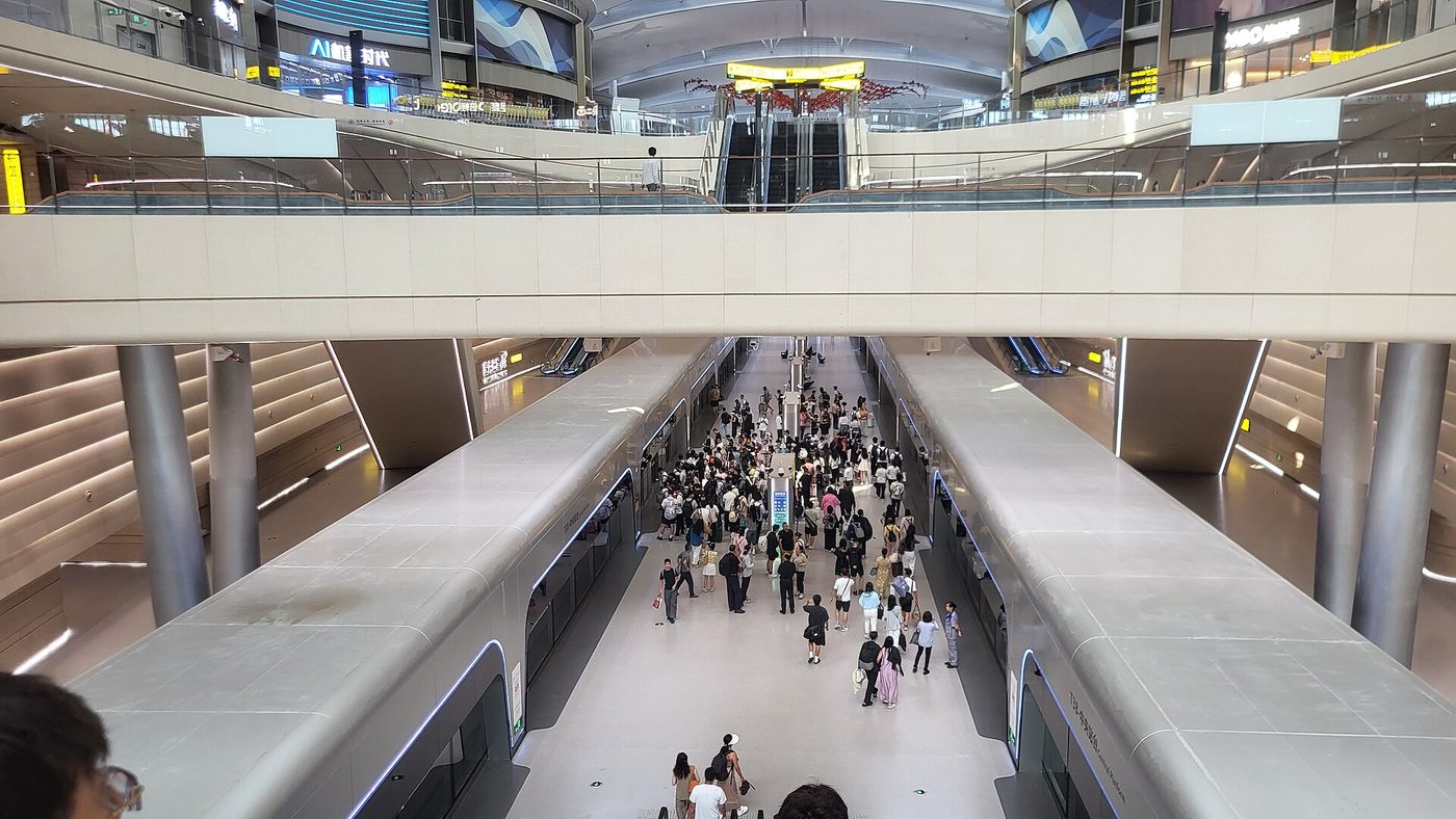 A modern rail platform in Chongqing in 2025, with two trains and passengers between them.