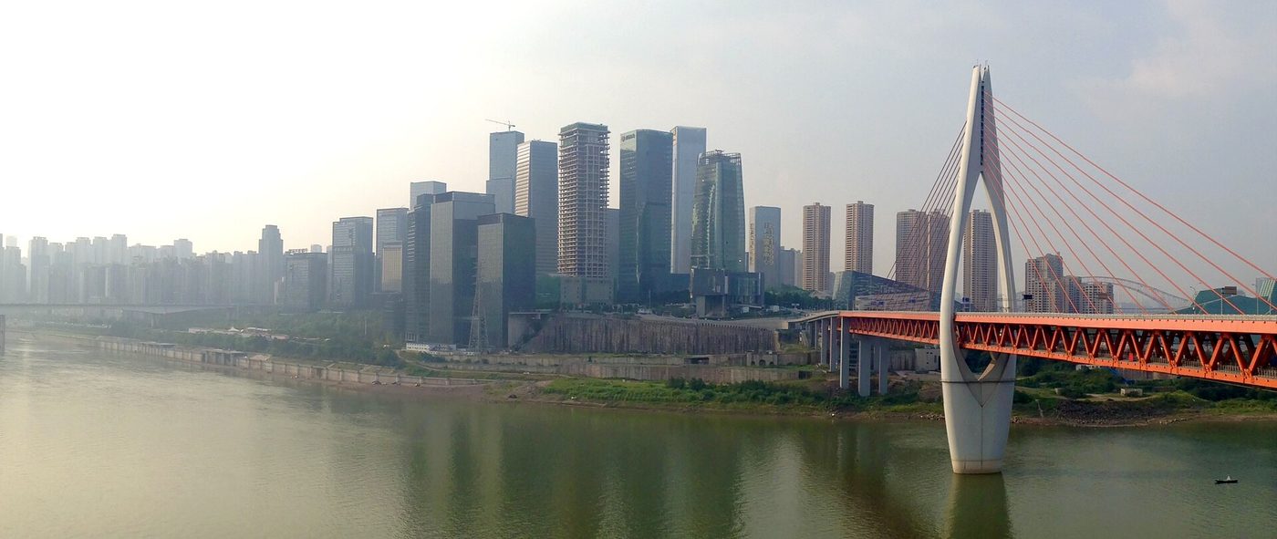 The Chongqing skyline rising above the Jialing River, with the orange Qiansimen Bridge in the foreground.